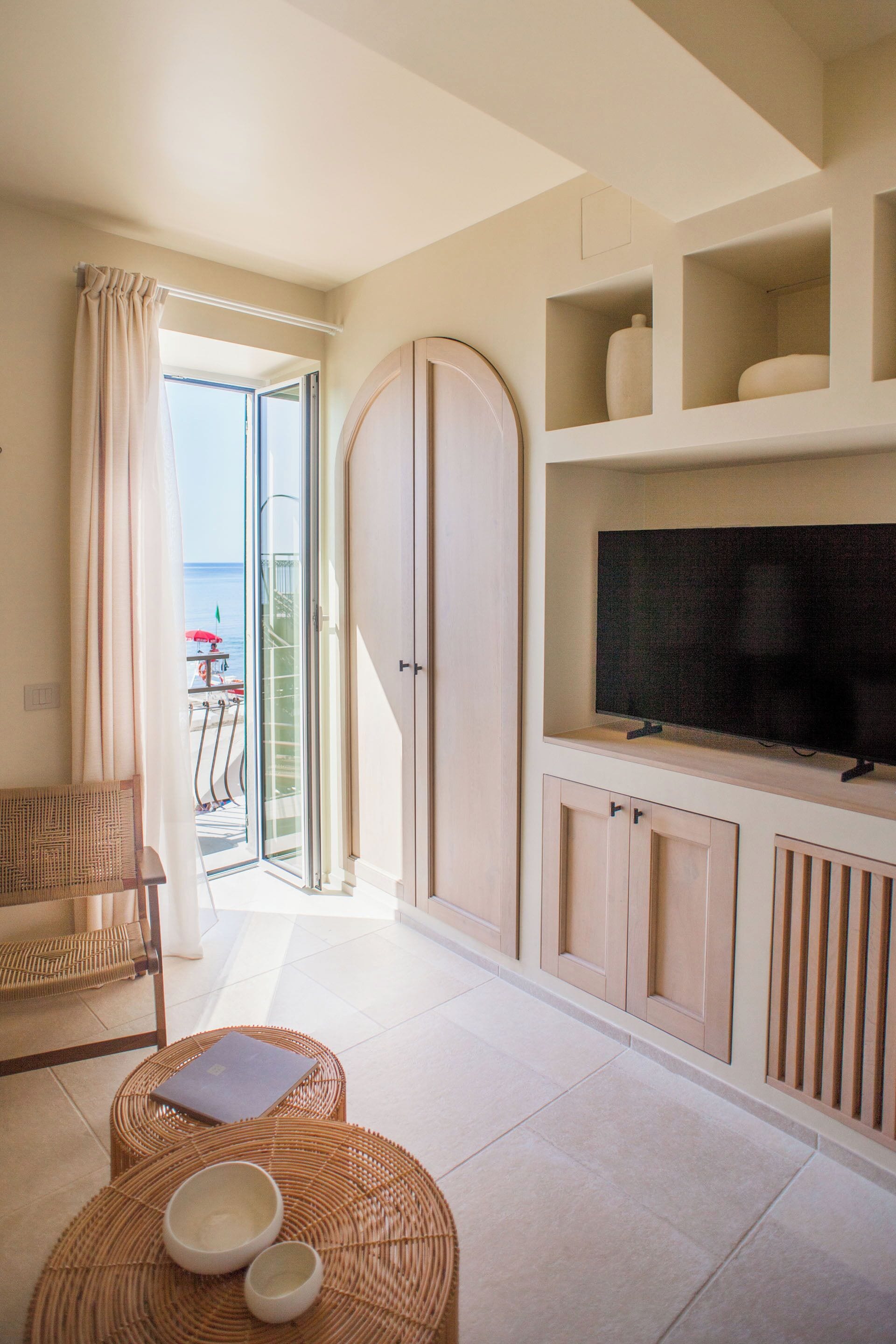 Una habitación con televisión sobre un mueble, muebles de mimbre y vista al mar.