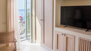 Una habitación con televisión sobre un mueble, muebles de mimbre y vista al mar.