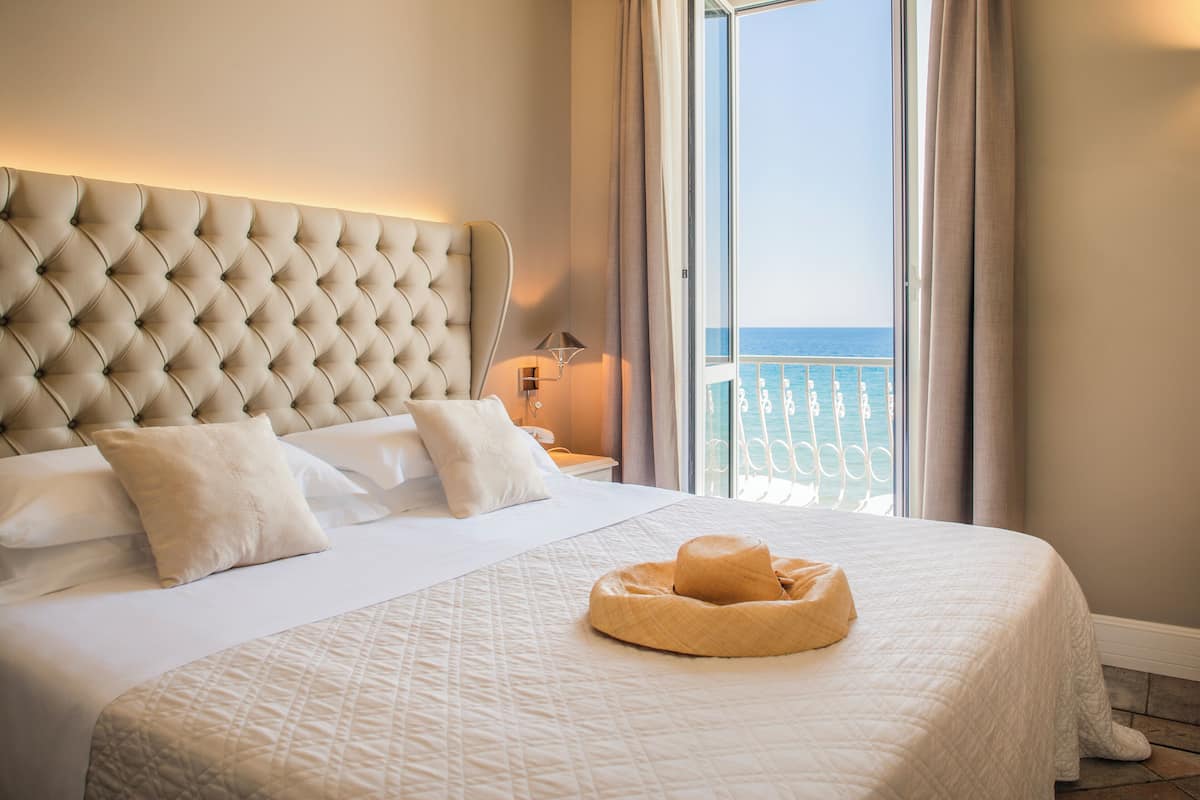 A hotel room with a large bed, a headboard, and a view of the sea through a balcony.