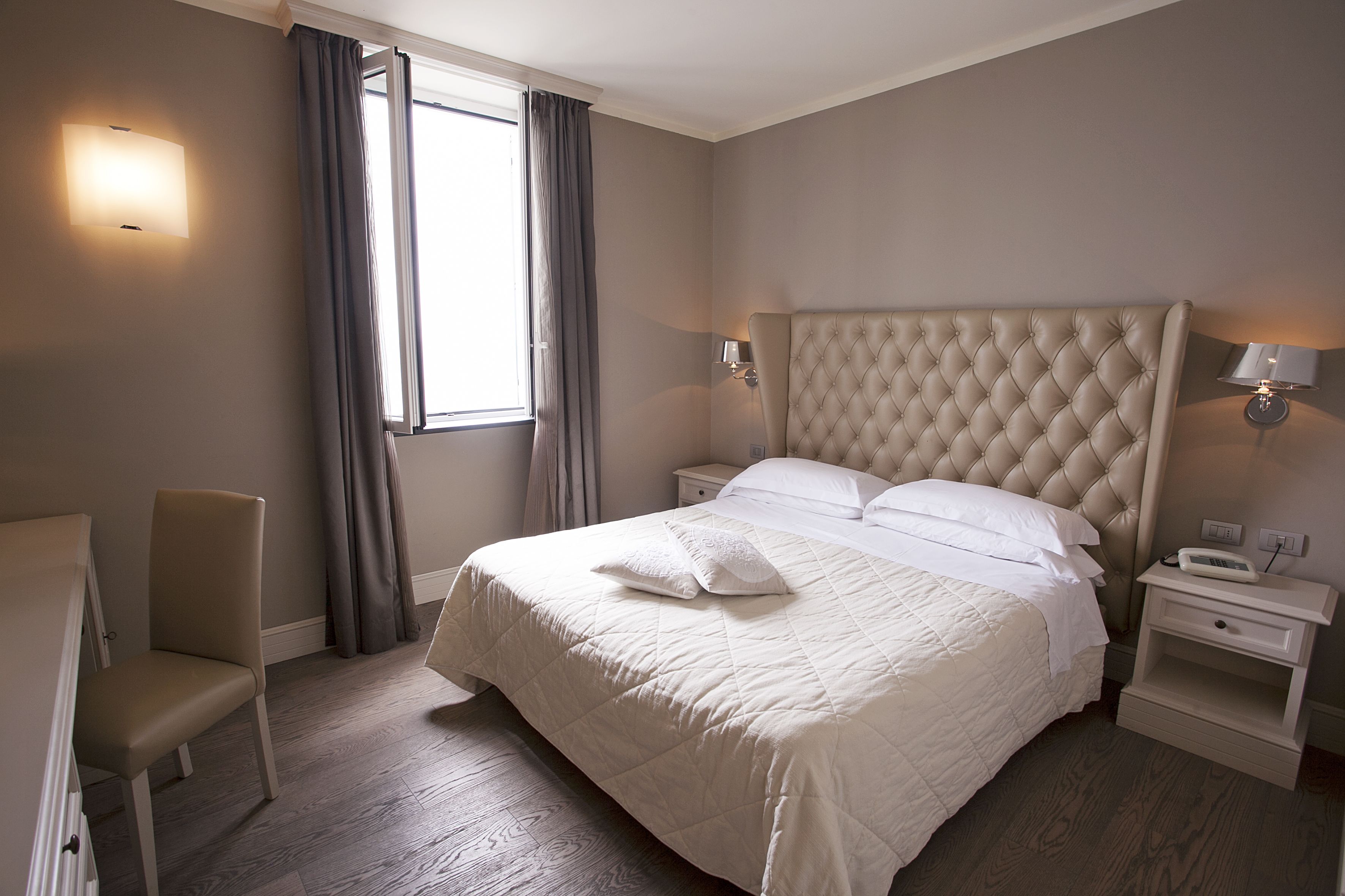 A hotel room with a large bed, a chair, a nightstand, and a bedside table.