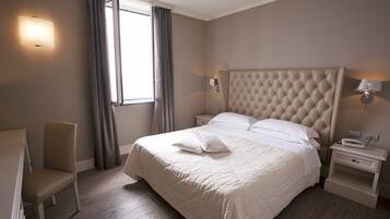 A hotel room with a large bed, a chair, a nightstand, and a bedside table.