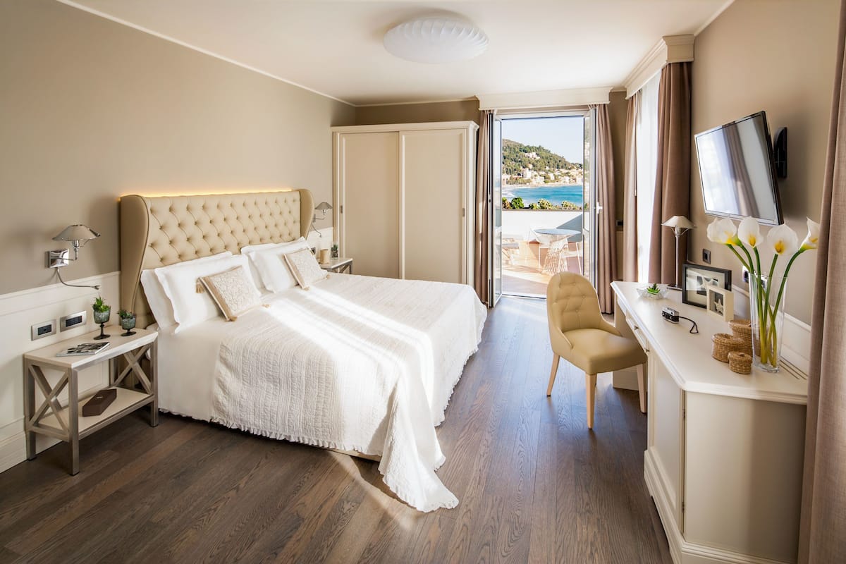 A hotel room with a large bed, a desk with a TV, and a view of the sea.