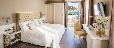 A hotel room with a large bed, a desk with a TV, and a view of the sea.
