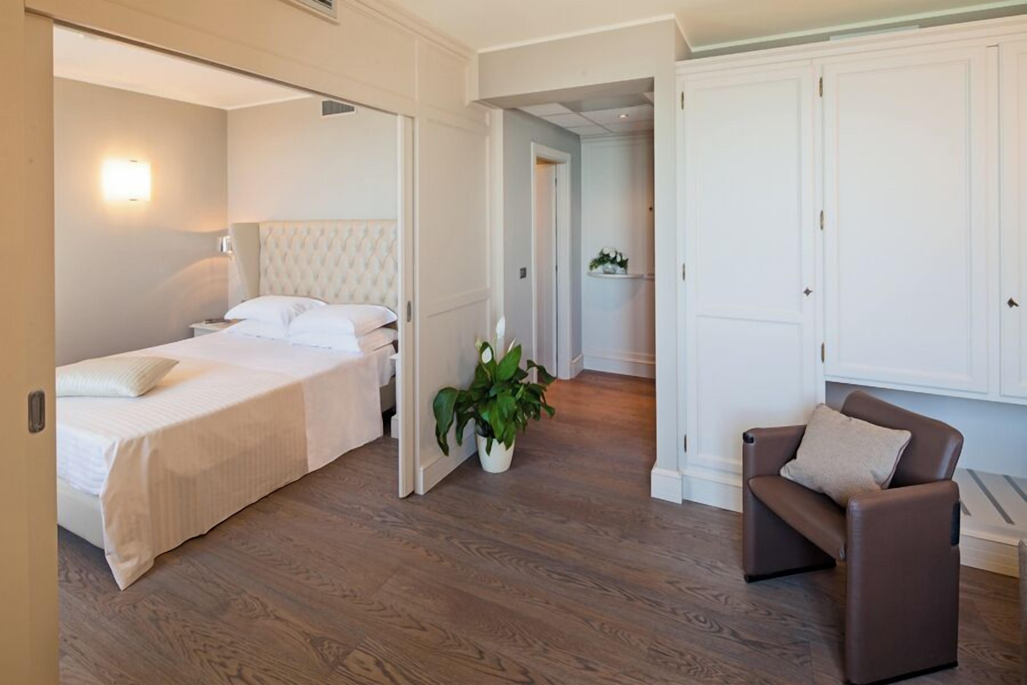 Ein Schlafzimmer mit einem Bett, einem Nachttisch, einer Topfpflanze, einem braunen Ledersessel und einem weißen Kleiderschrank.