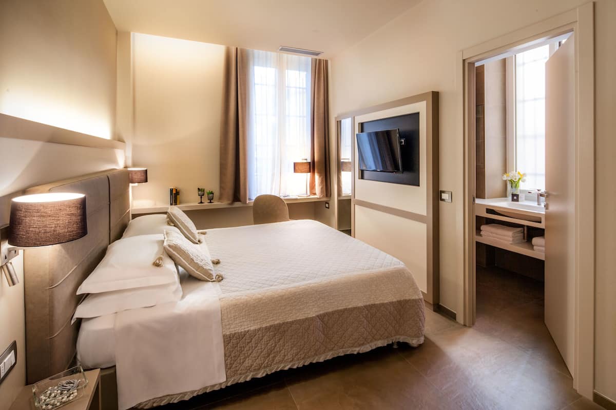 A hotel room with a bed, bedside lamp, telephone, and a TV mounted on the wall.