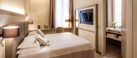 A hotel room with a bed, bedside lamp, telephone, and a TV mounted on the wall.