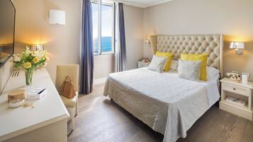 Een hotelkamer met een groot bed, nachtkastjes, een bureau met stoel, een vaas met bloemen en een raam met gordijnen.