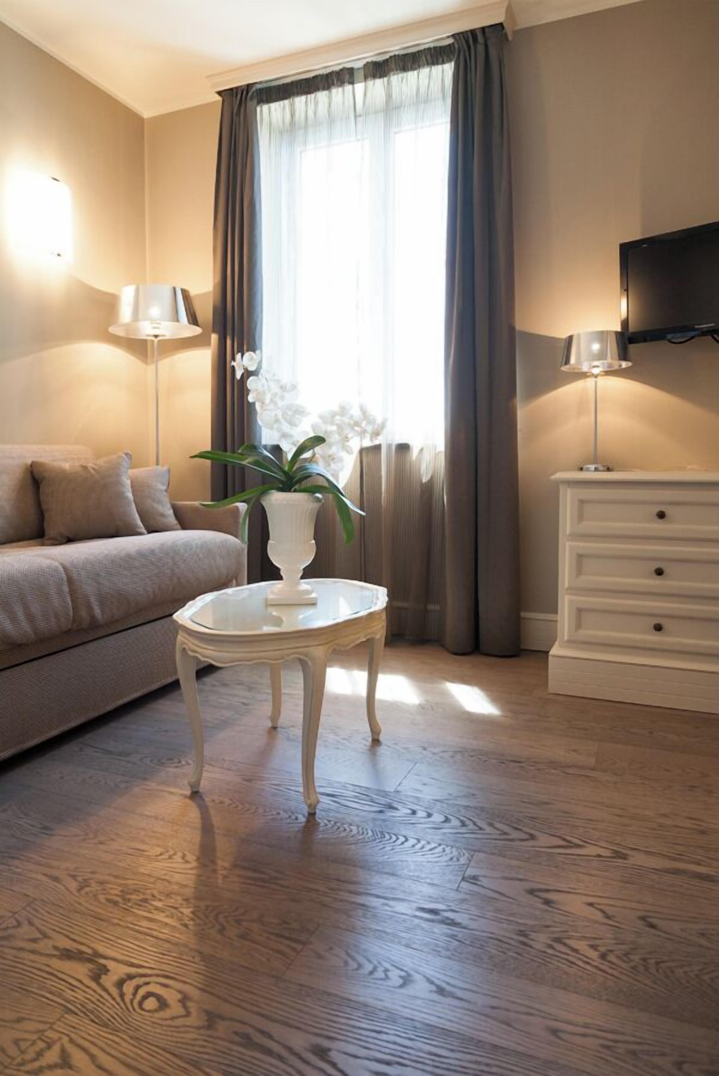A hotel room with a sofa, a small table with a vase, a dresser, and a TV mounted on the wall.