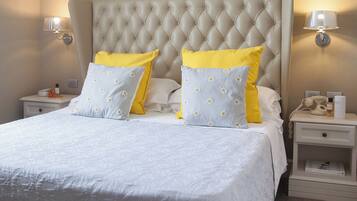 A bedroom with a tufted headboard, a bed with white bedding and yellow pillows, bedside tables with lamps, and a wooden floor.