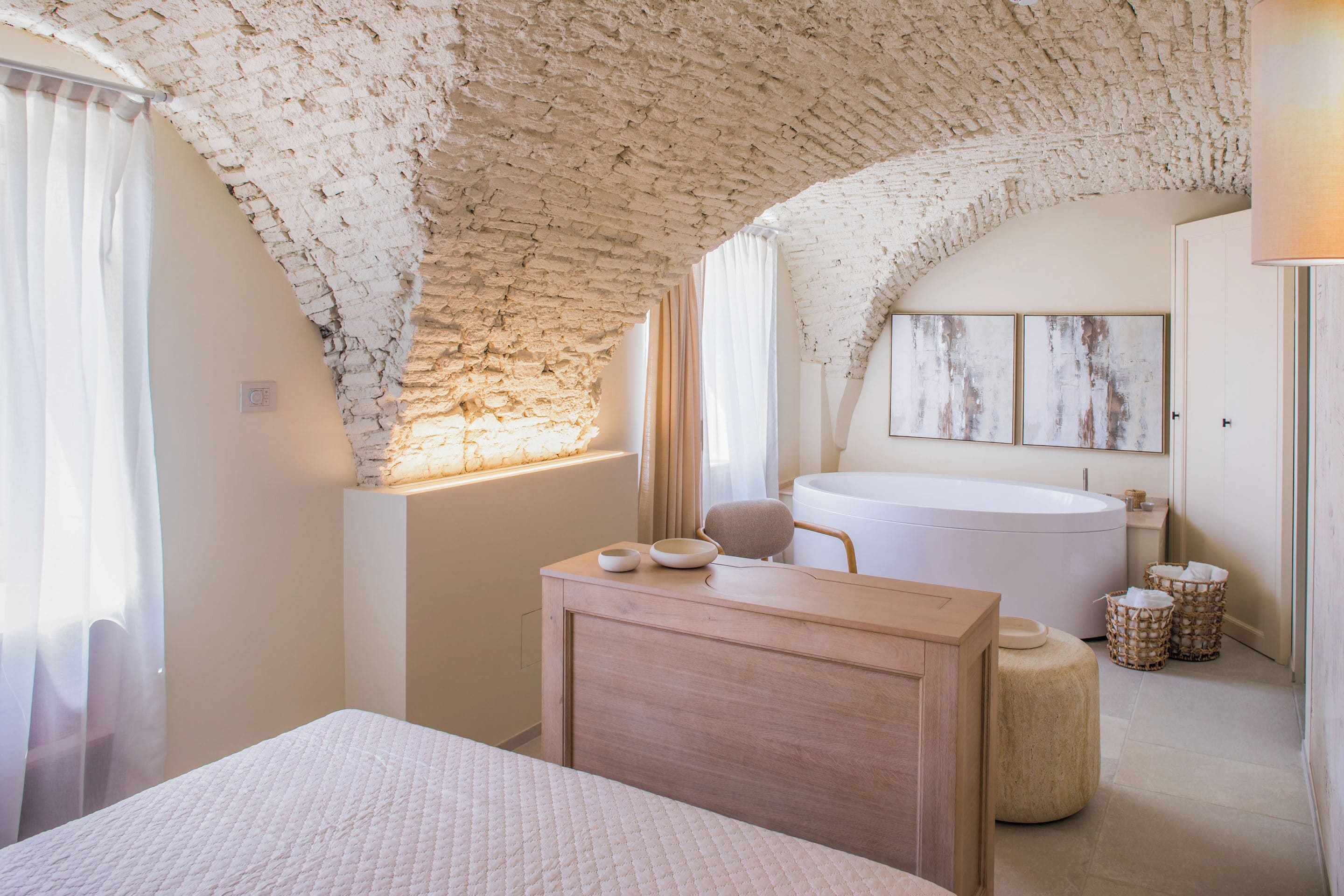 Une chambre à coucher avec un grand lit, une commode en bois, une baignoire et un plafond en pierre.