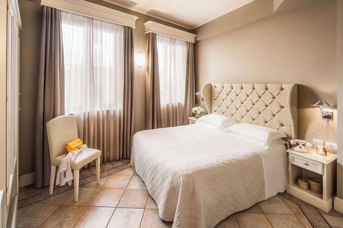 A neatly arranged hotel room with a large bed, a chair, a nightstand, and curtains.