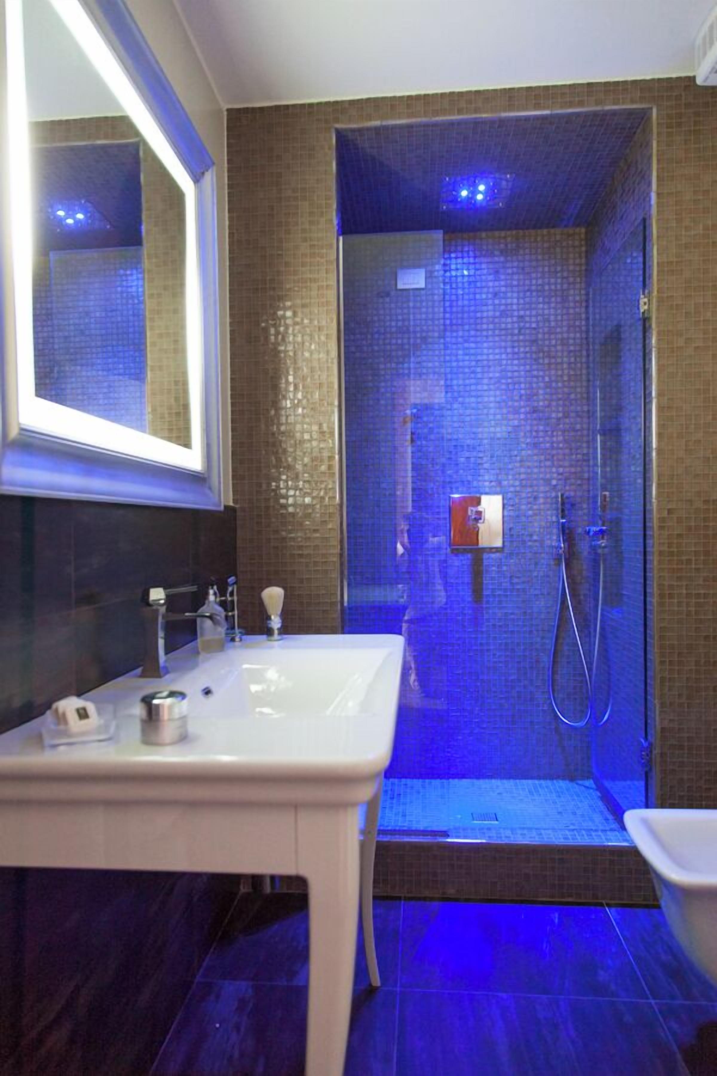 A bathroom with a white sink, a mirror, a shower with a glass door, and a tiled floor.