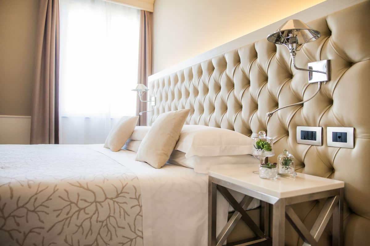 A hotel room with a tufted headboard, a bedside table with a lamp, and a bed with white linens.