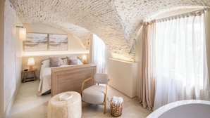 Un dormitorio con cama, mesitas de noche, una silla, un taburete pequeño, una cesta y una bañera.