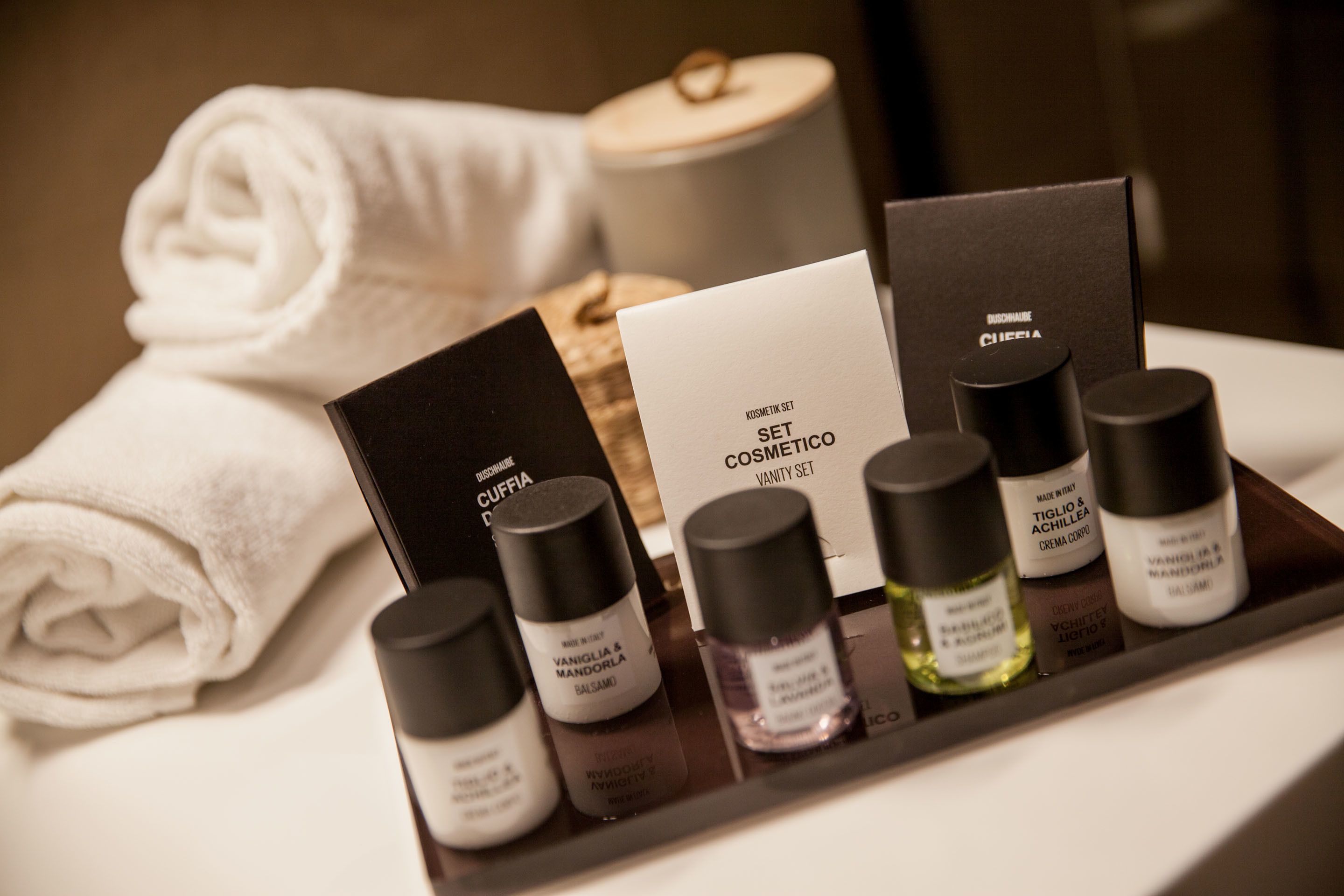 A tray with various cosmetic products, a folded towel, and a candle in a hotel setting.