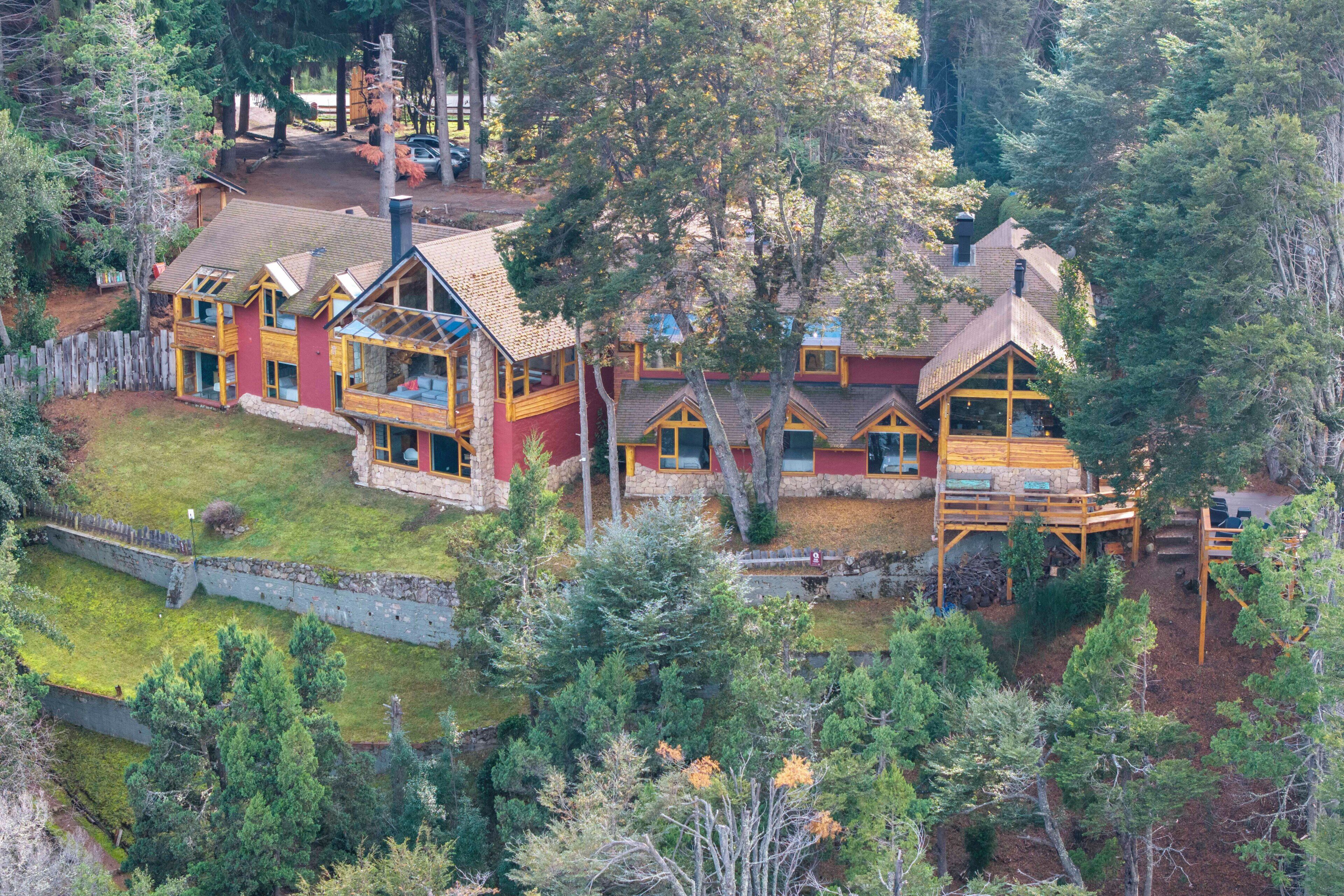 Un chalet à étages doté d’une cheminée centrale, entouré d’une forêt dense.