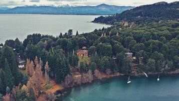 Vista aérea de una zona costera con un lago, colinas boscosas y un pequeño poblado con casas y un muelle.