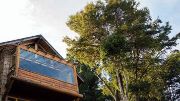 A cabin with a stone exterior, a wooden balcony, and a large glass window.