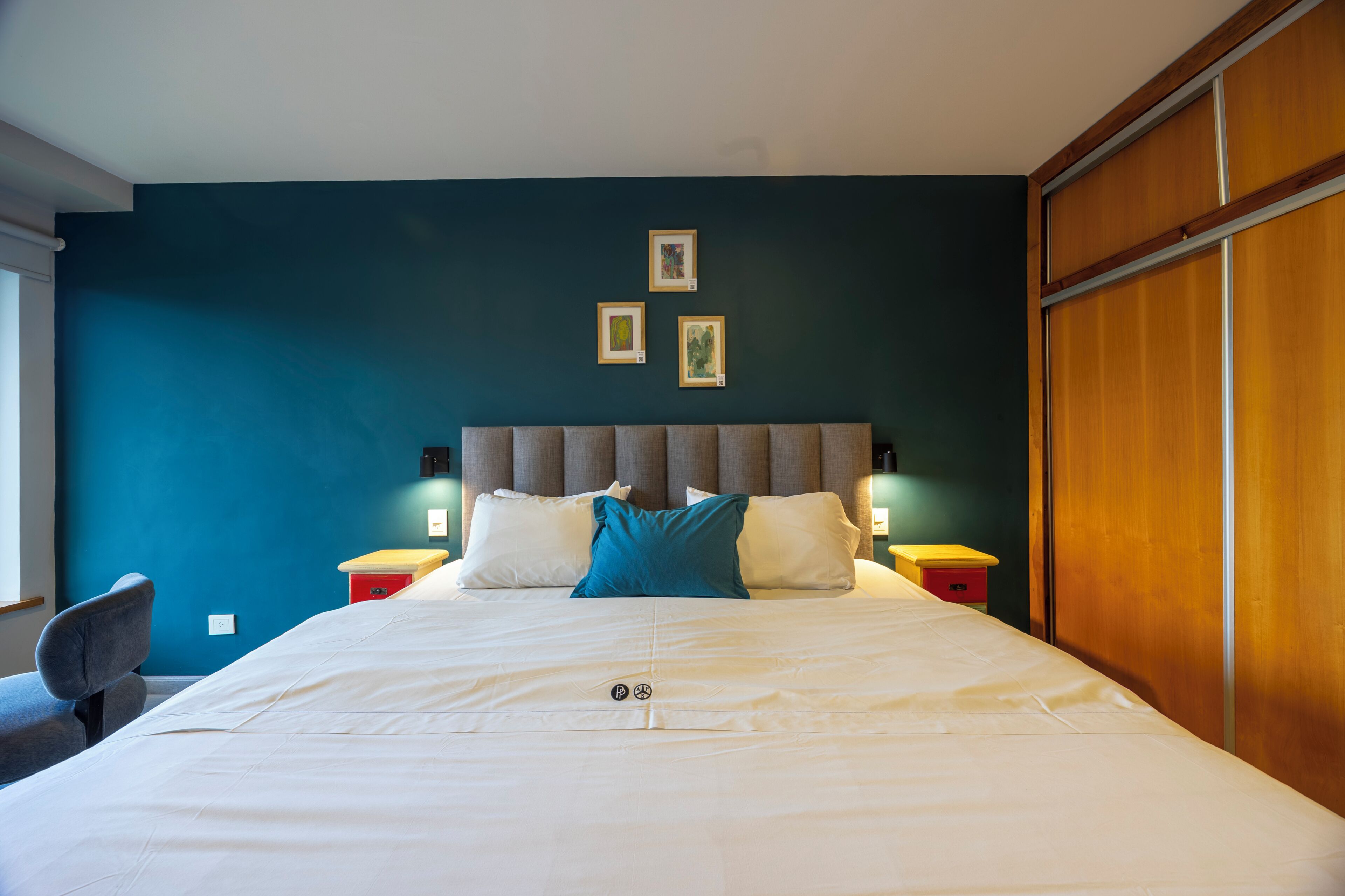 Un dormitorio con cama, cabecera, mesitas de noche y decoración en la pared.