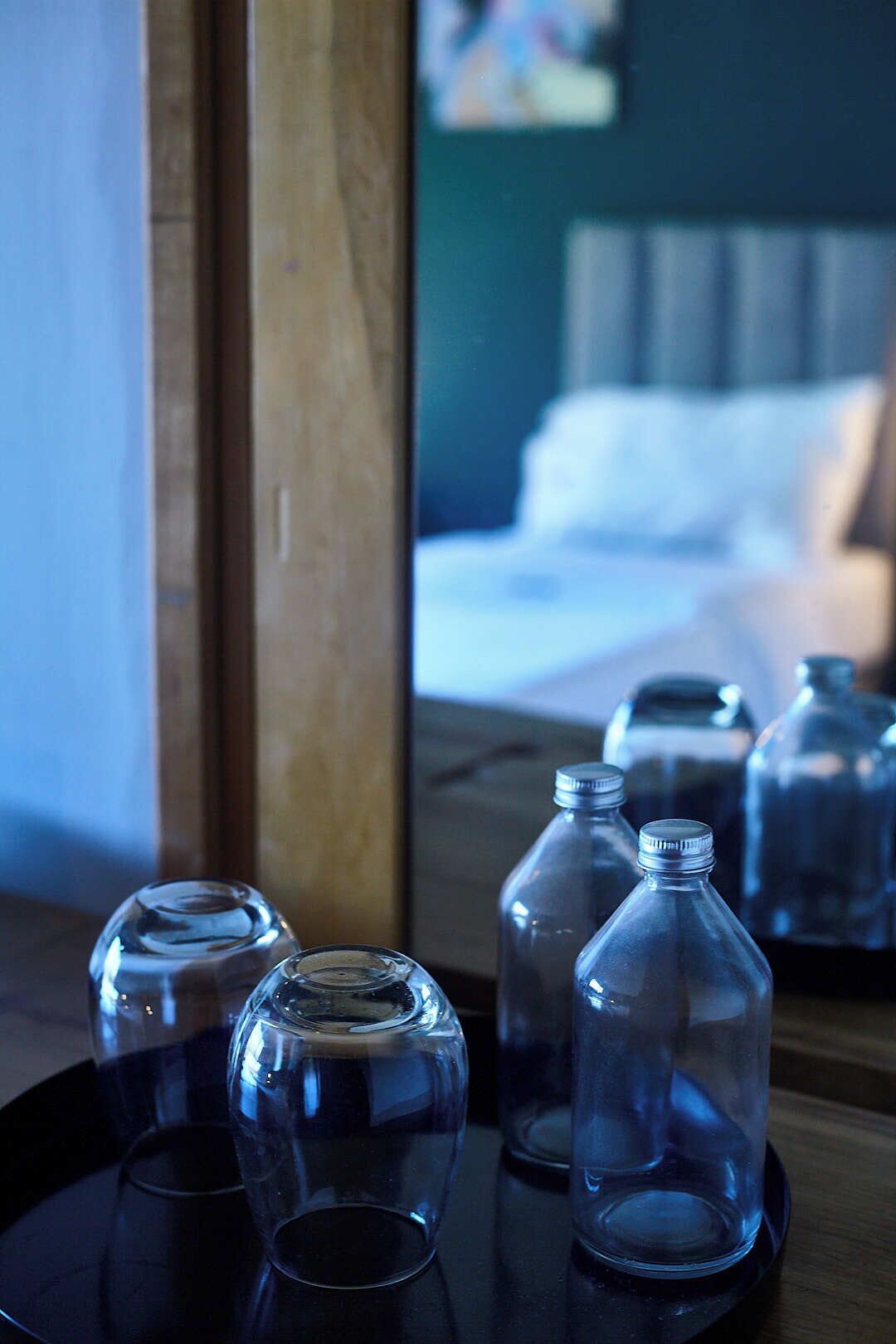 A room with a bed, a wooden side table, and clear glass bottles on the table.