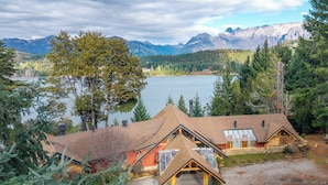 Una cabaña de techo inclinado, con chimenea visible y vista a un lago y montañas.
