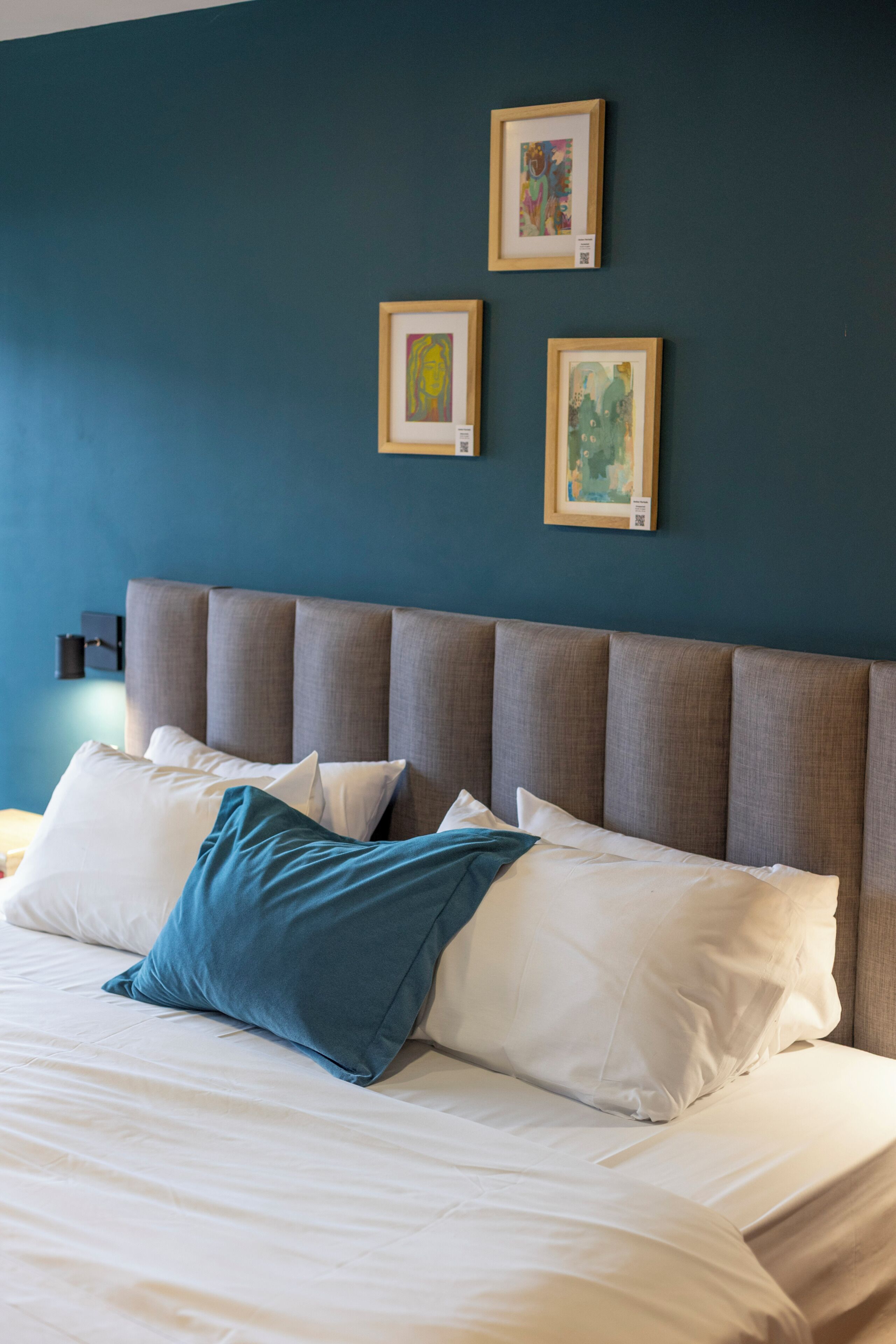 A neatly made bed with a headboard, white and blue pillows, and framed artwork on the wall.