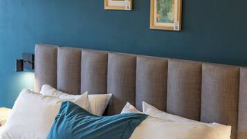 A neatly made bed with a headboard, white and blue pillows, and framed artwork on the wall.