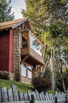 A two-story log cabin with a stone foundation, large windows, and a balcony.