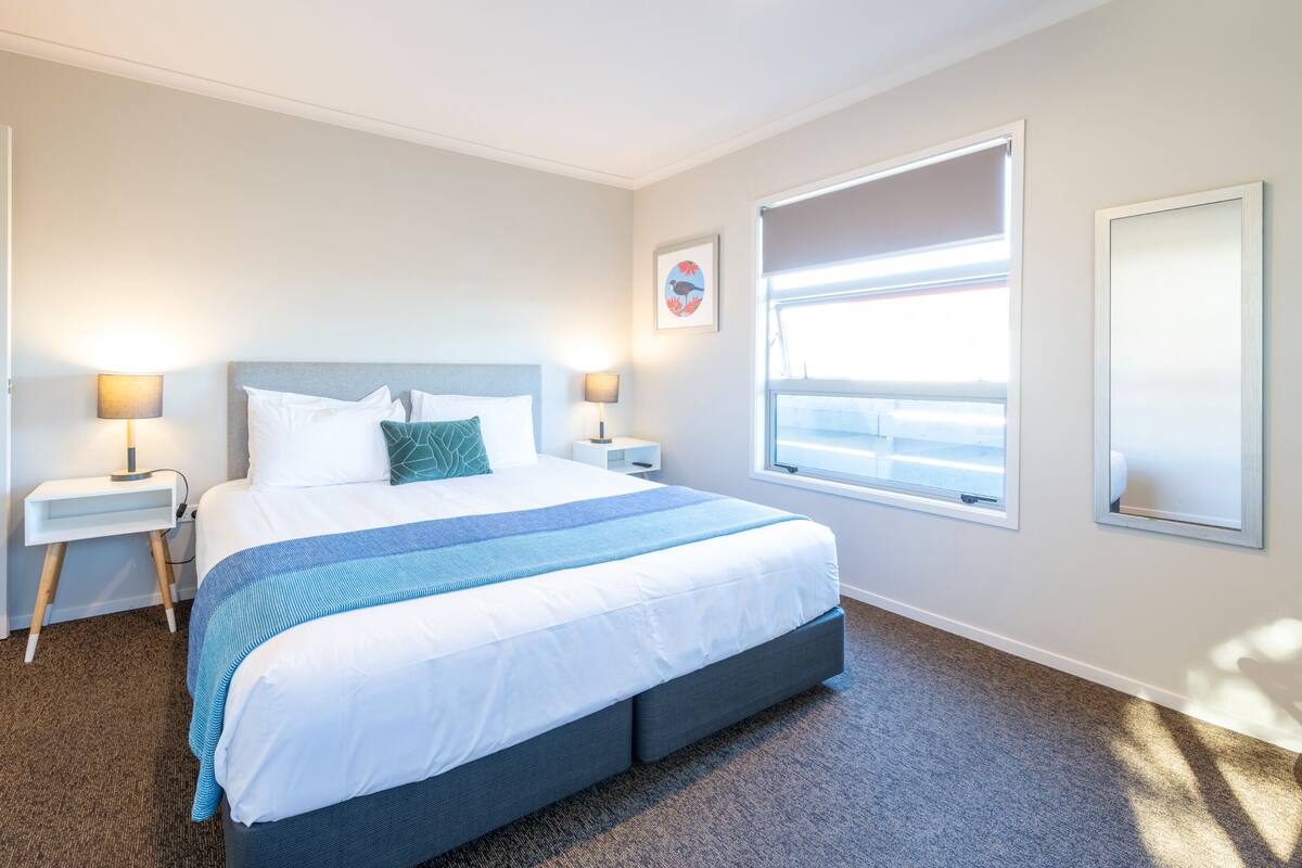 A hotel room with a bed, bedside tables, a window, and a wall-mounted mirror.