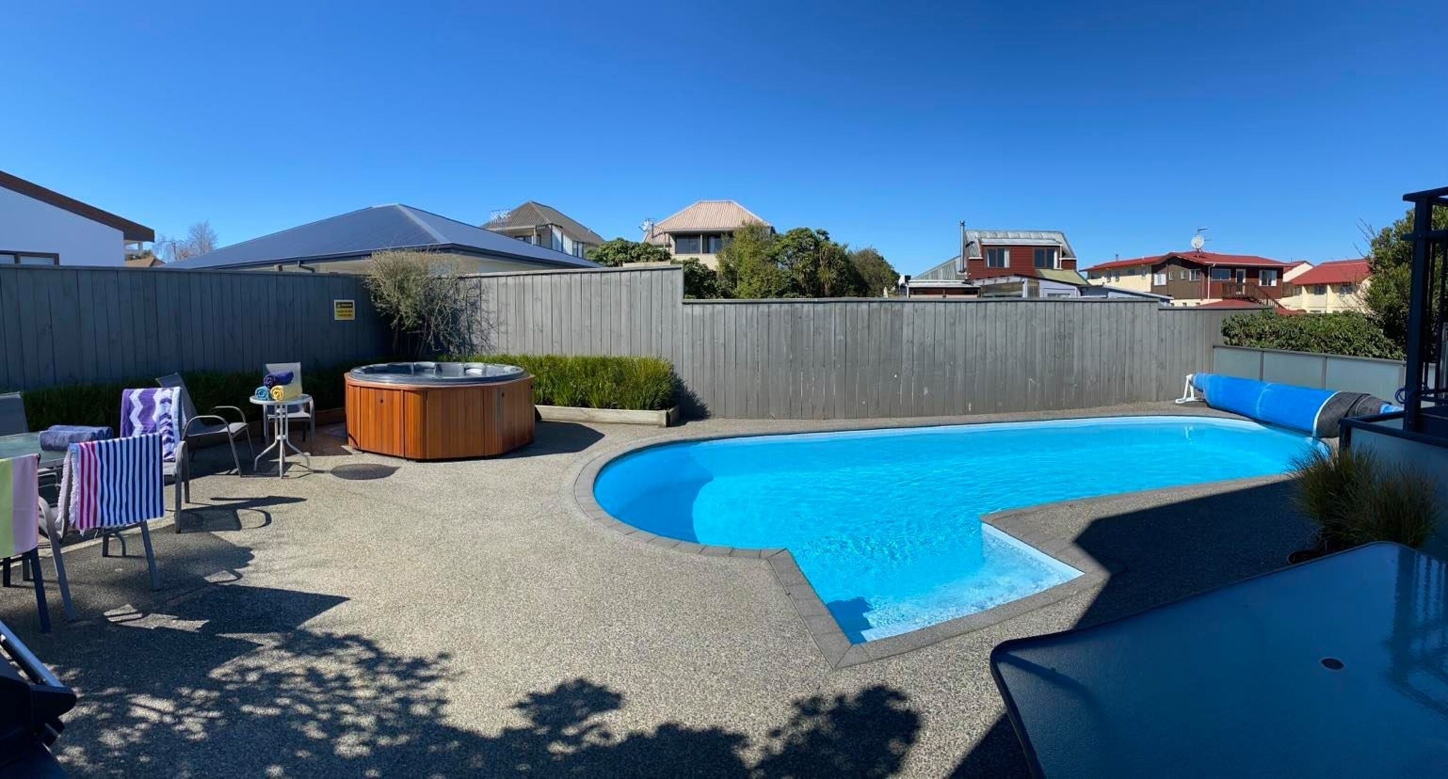 A backyard with a swimming pool, a hot tub, and a covered seating area.