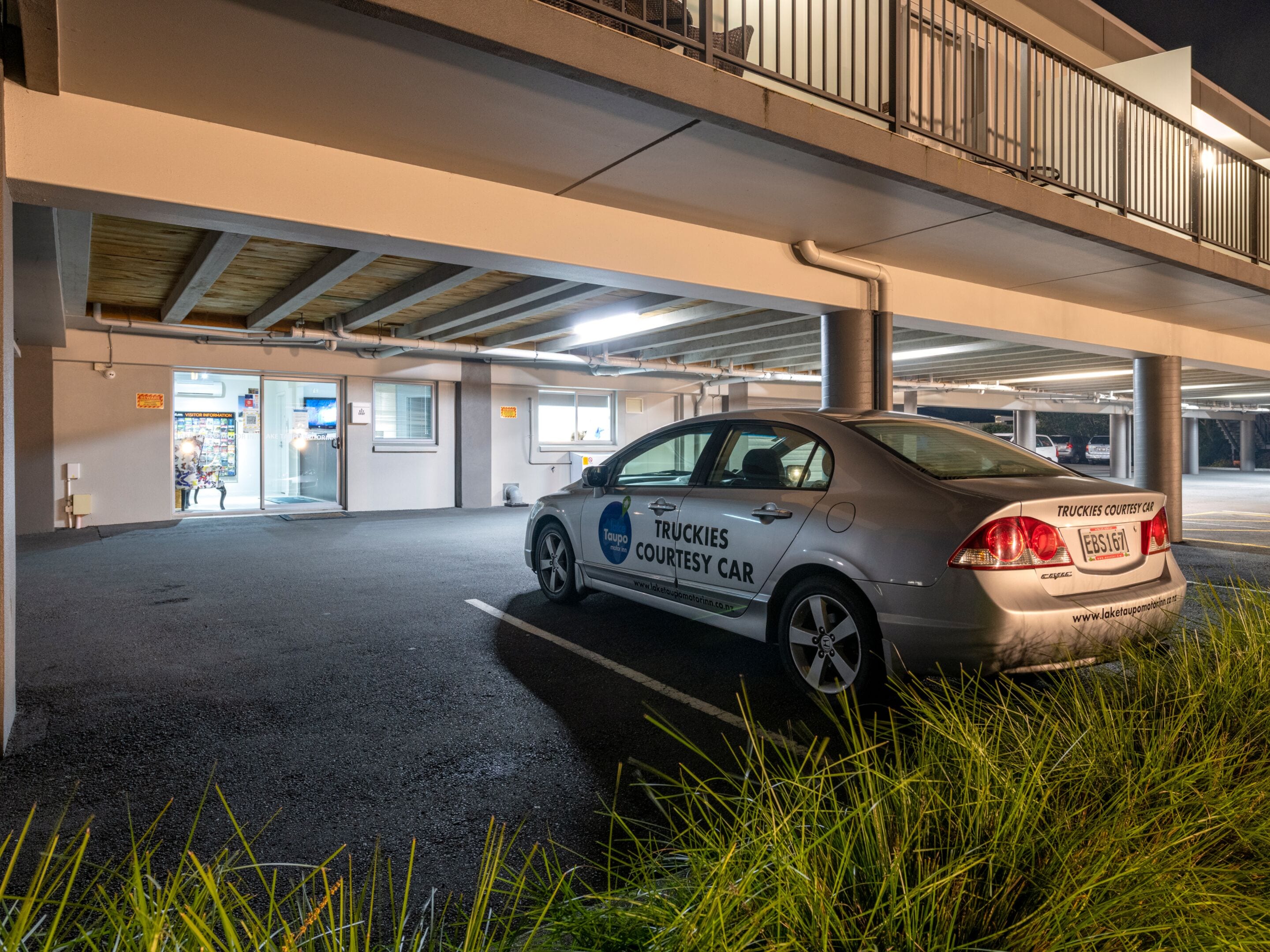 A parking garage with a car labeled "TRUCKIES COURTESY CAR" parked under an overpass.
