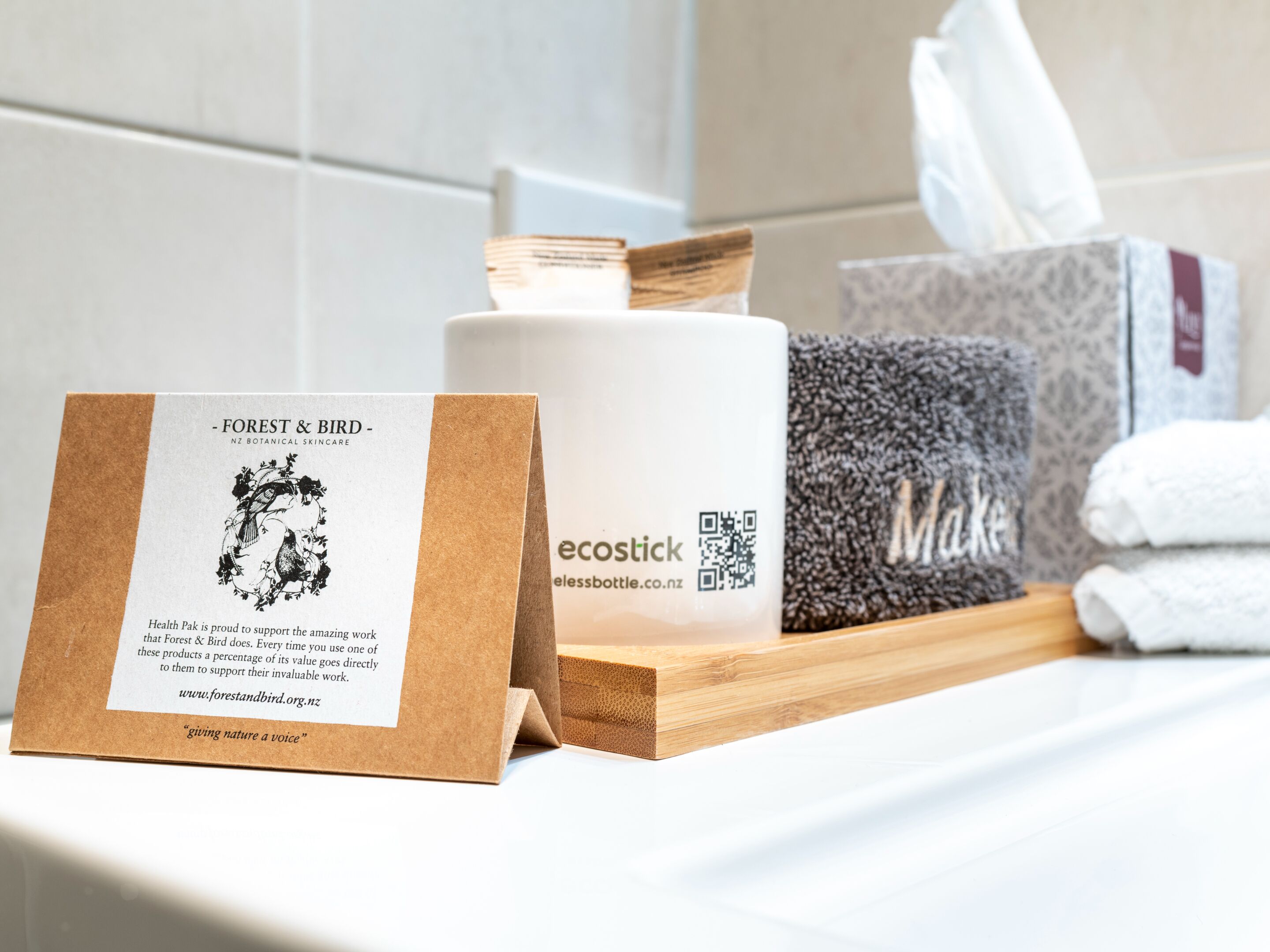 A bathroom counter with a tissue box, a bottle of shampoo, and a card from 'Forest & Bird NZ Botanical Skincare'.
