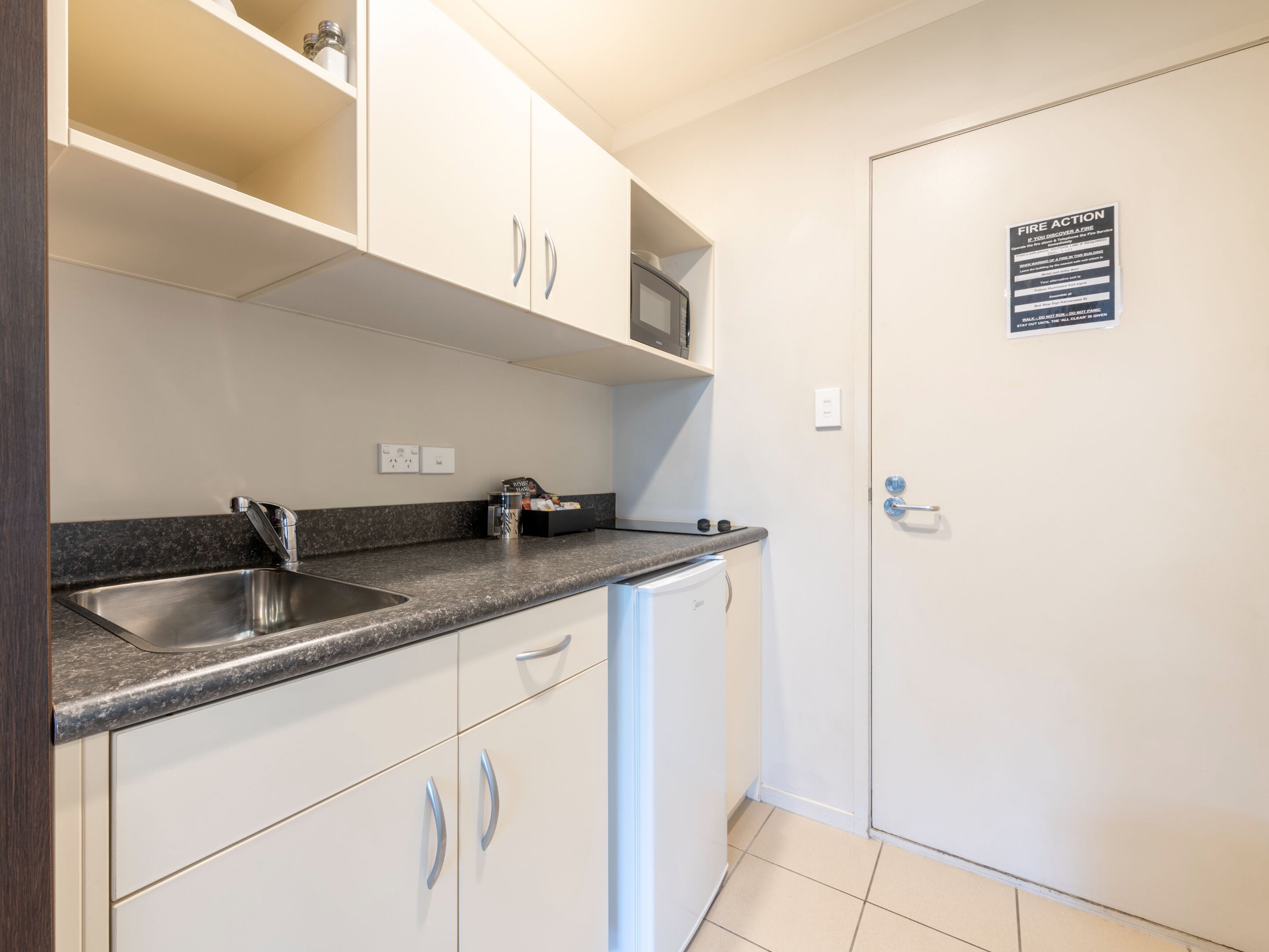 A modern kitchen with white cabinets, a stainless steel sink, a microwave, and a compact refrigerator.