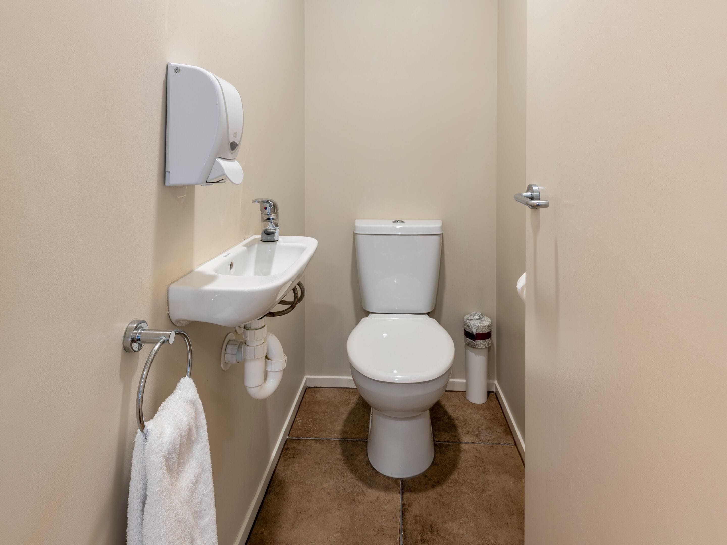 Une petite salle de bain propre, avec un lavabo, des toilettes et un porte-serviettes, le tout de couleur blanche.