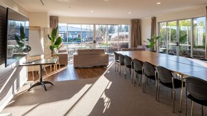 A modern hotel room with a large window, a sofa, a dining table, and a TV. - Lake Taupo Motor Inn (Taupo)