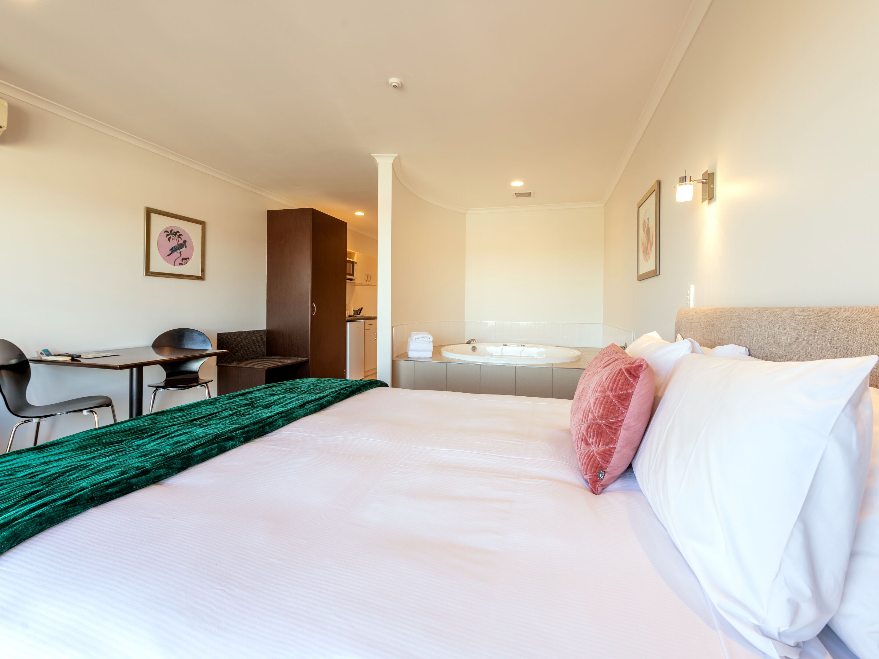 A hotel room with a bed, a desk, a chair, a bathroom with a sink and bathtub, and a door leading to a kitchenette.