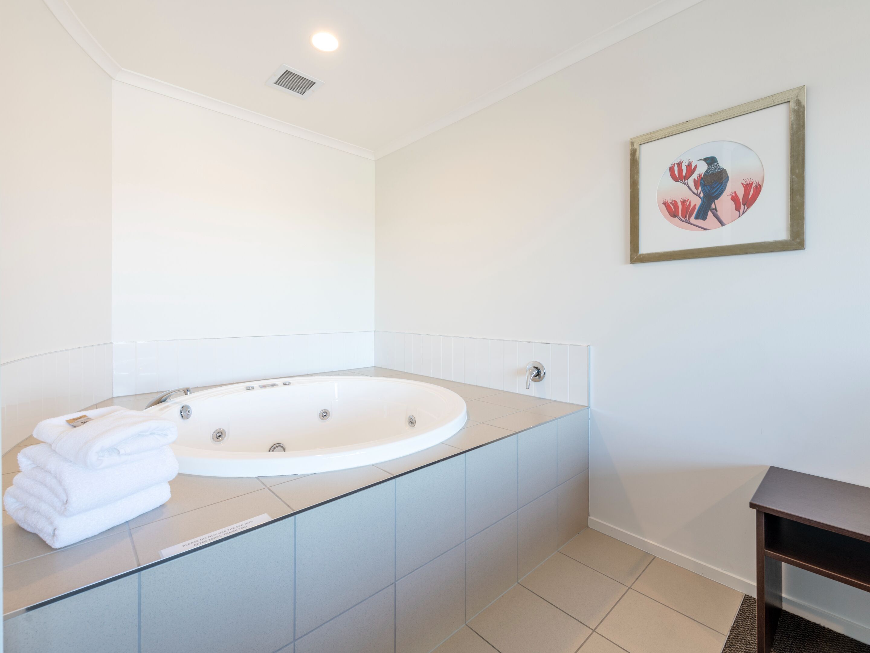 A modern bathroom with a freestanding bathtub, a framed artwork on the wall, and a stack of towels on the counter.