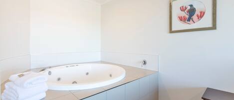 A modern bathroom with a freestanding bathtub, a framed artwork on the wall, and a stack of towels on the counter.