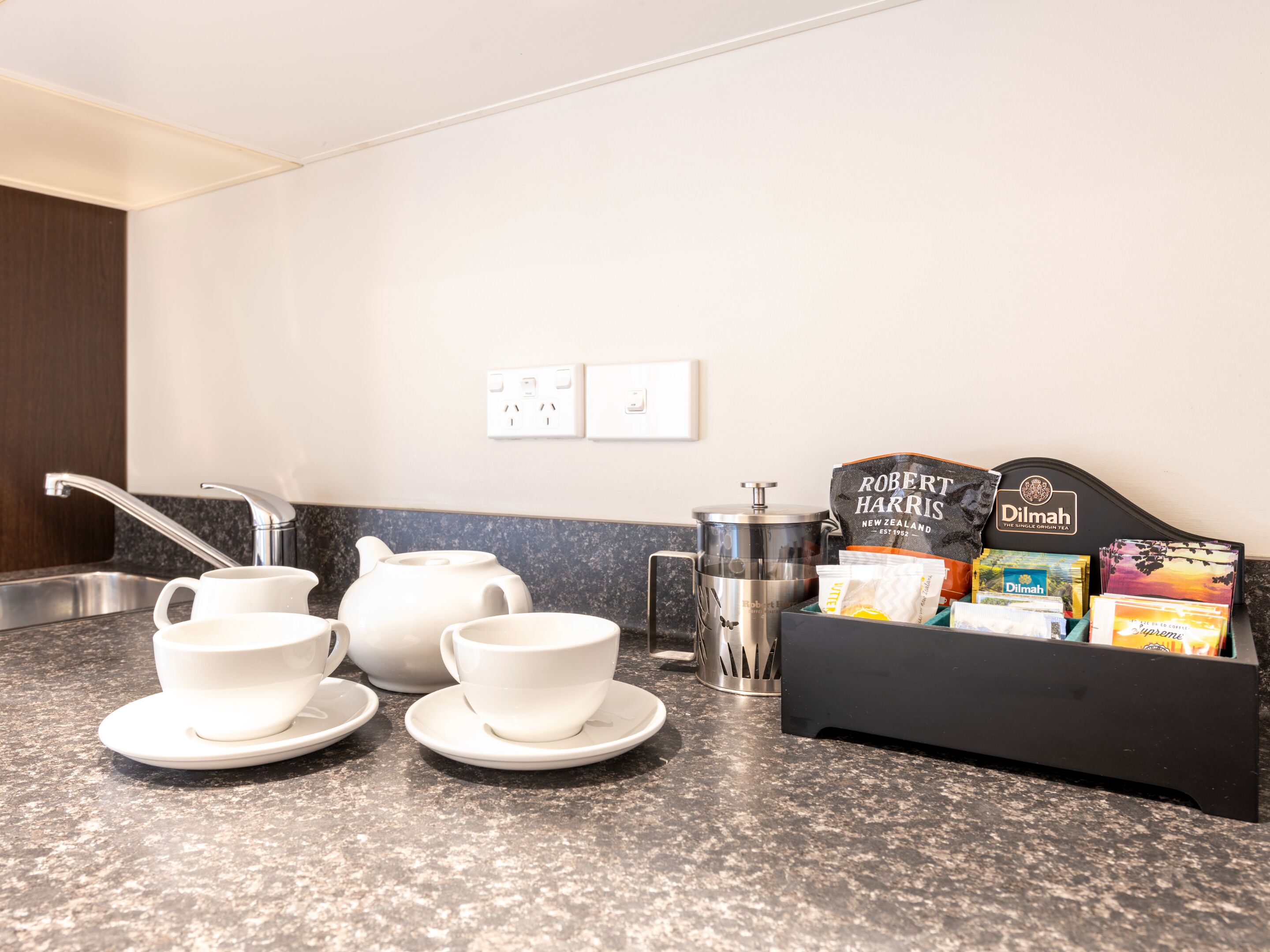 A kitchen counter with white teapots, cups, and a coffee maker. There are tea bags and a tea box labeled "Robert Harris" and "Dilmah".