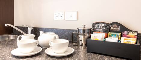 A kitchen counter with white teapots, cups, and a coffee maker. There are tea bags and a tea box labeled "Robert Harris" and "Dilmah".
