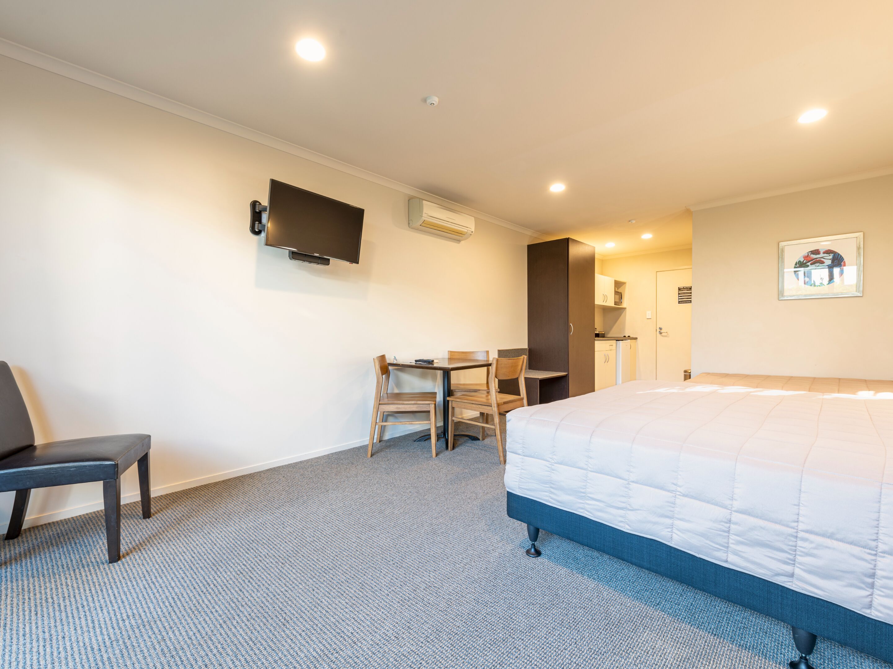 Habitación de hotel con cama, escritorio, dos sillas, televisor y kitchenette.