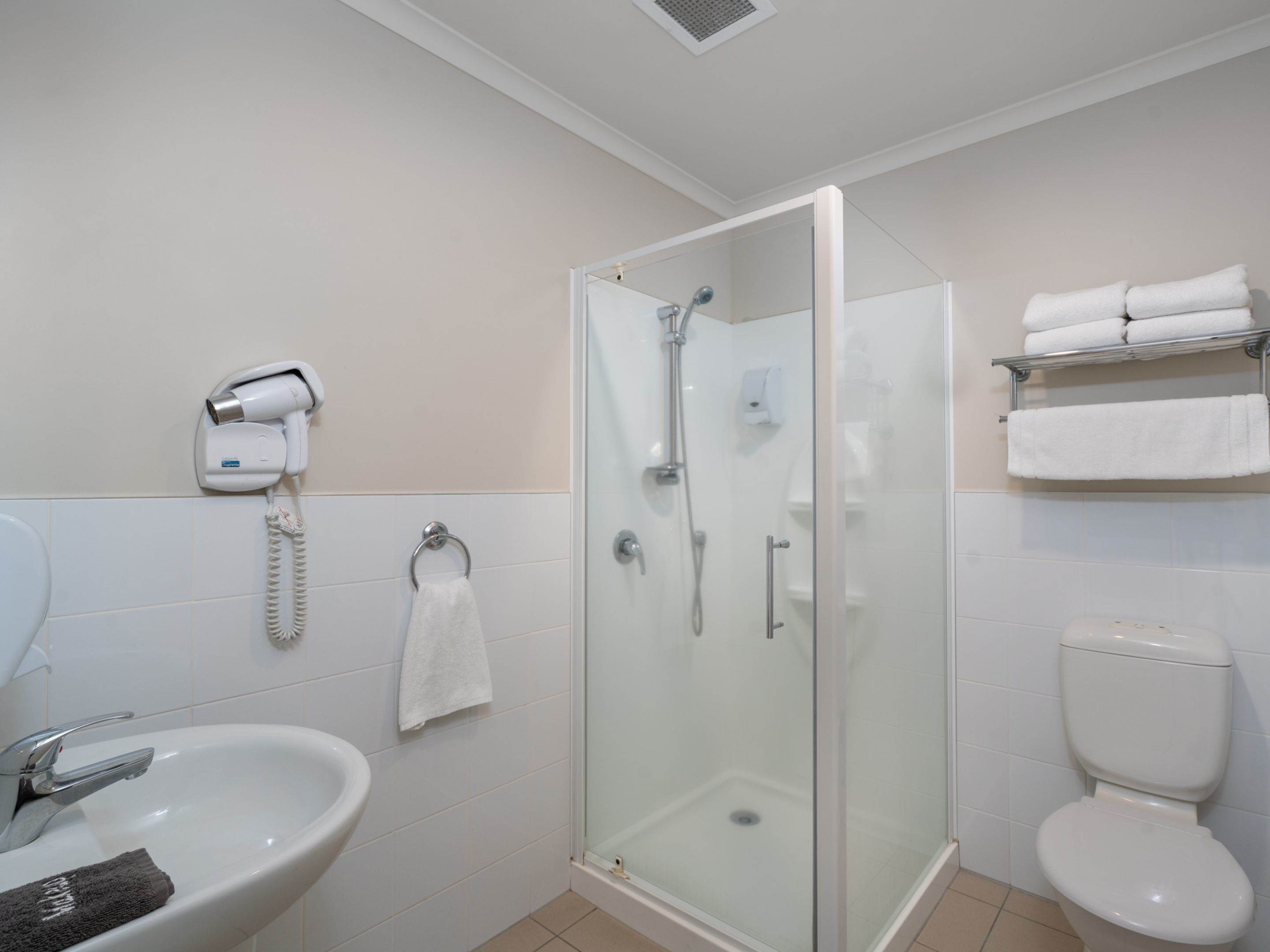 A modern bathroom with a glass-enclosed shower, a sink, a toilet, and a towel rack with folded towels.