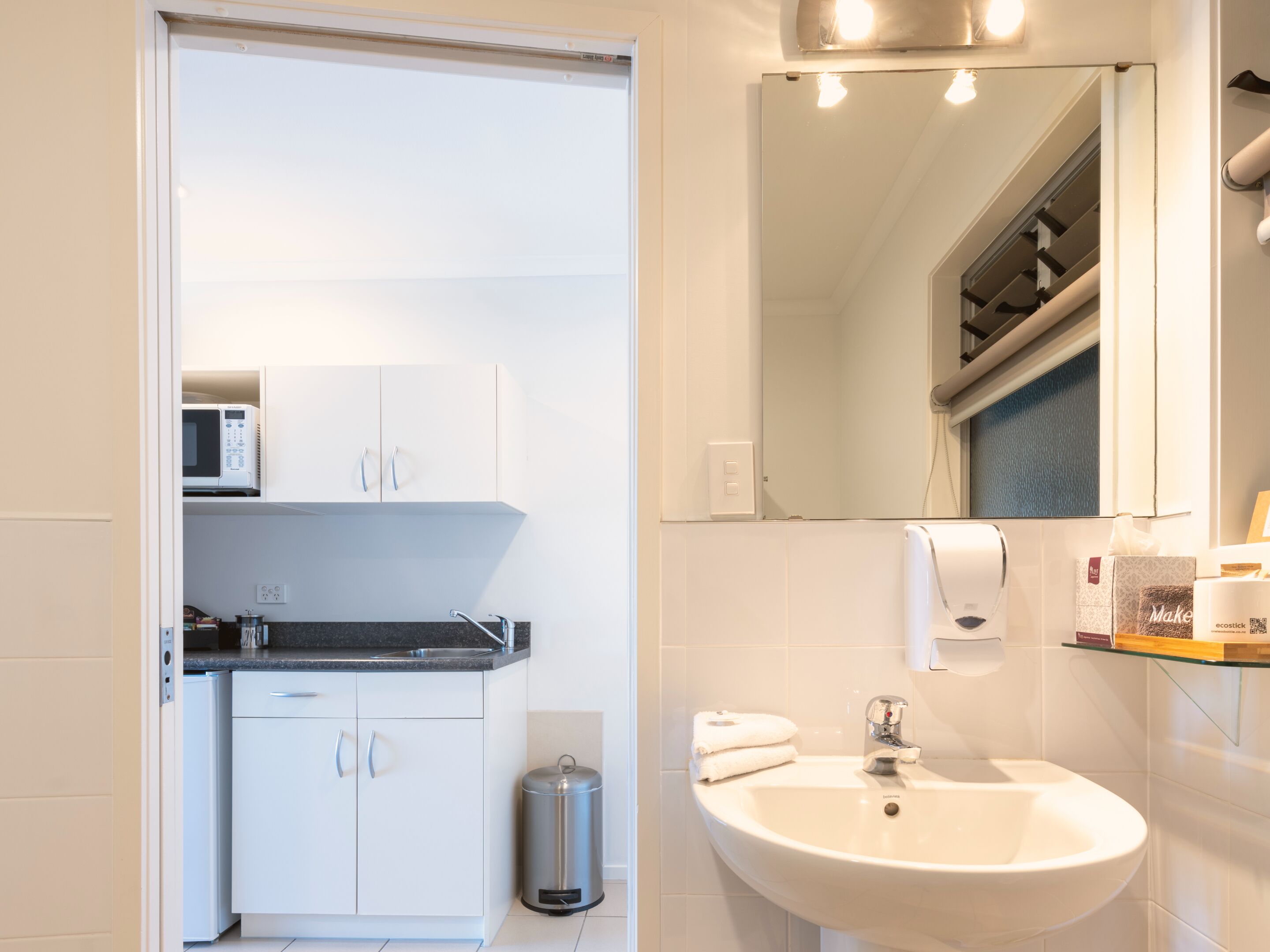 Un baño moderno con un lavamanos blanco, un espejo, un perchero para toallas y un cesto de basura.