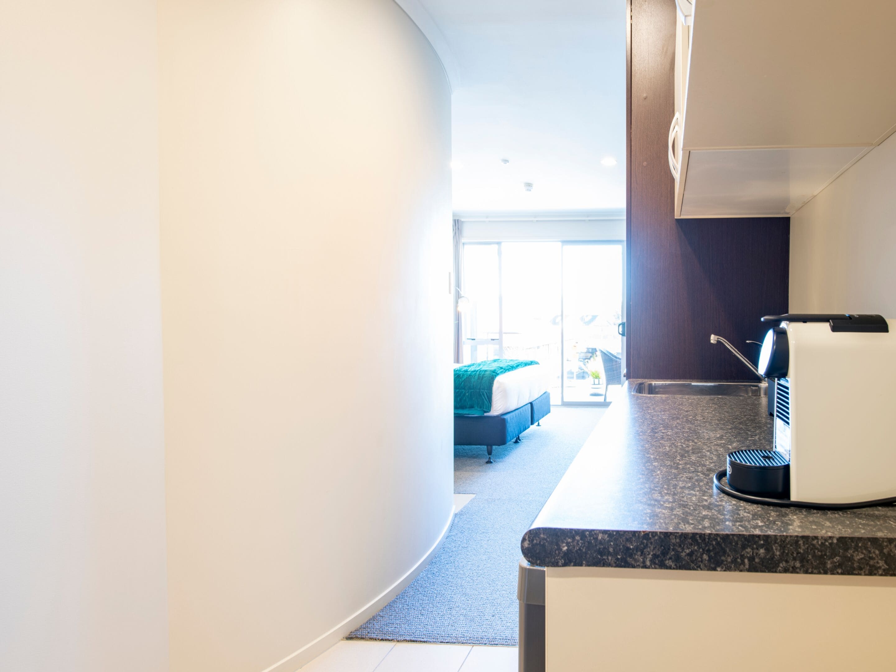 Una habitación de hotel moderna con cocina, una cama con cabecera azul y vistas al exterior.
