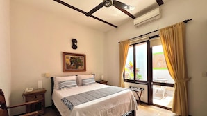 A hotel room with a bed, bedside tables, a ceiling fan, an air conditioning unit, a window with curtains, and a painting on the wall. - San Antonio Hotel Boutique (Cali)