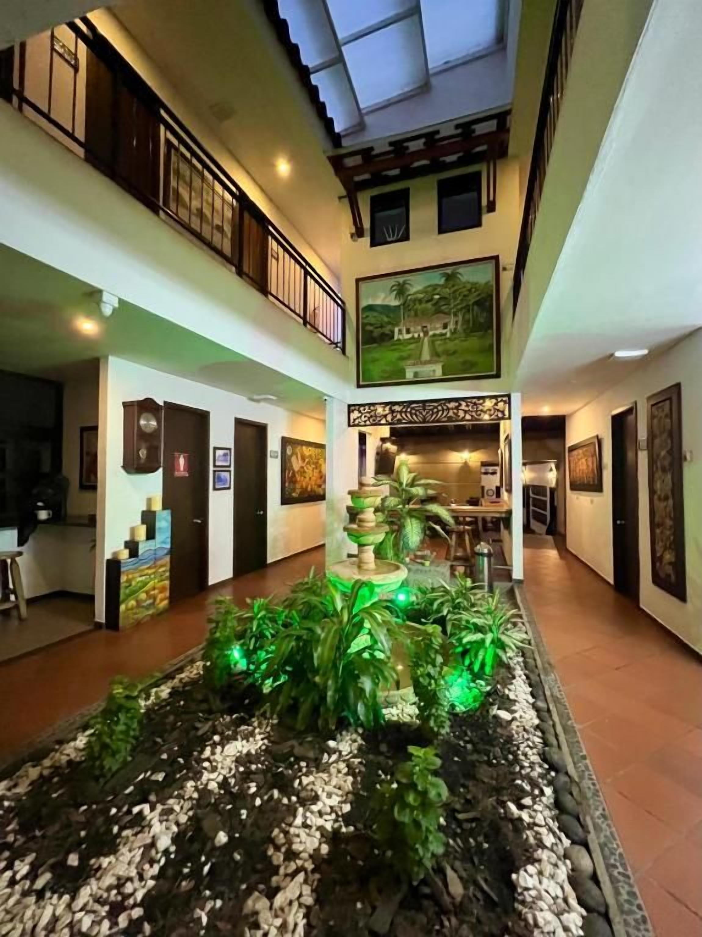 A hotel lobby with a central fountain, a second-floor balcony, and artwork on the walls.