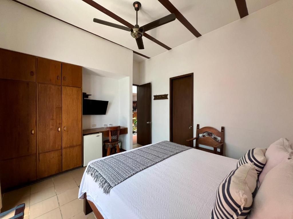 A bedroom with a bed, a wooden wardrobe, a television, and a ceiling fan.