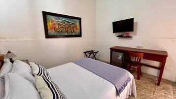 Una habitación de hotel con una cama, un escritorio, un televisor y un cuadro en la pared.
