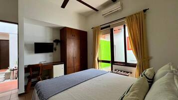 Habitación de hotel con cama, escritorio, silla, televisor, ventilador de techo y ventana con cortinas.