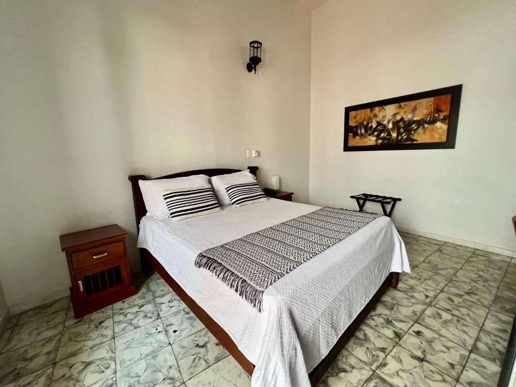 Un dormitorio con cama, mesita de noche, lámpara de pared y un cuadro enmarcado.
